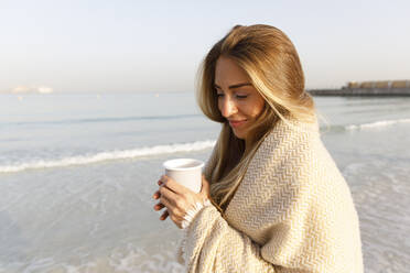 Lächelnde blonde Frau hält Teetasse am Strand - TYF00094