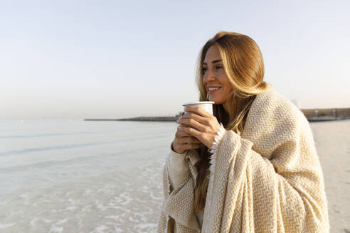 Glückliche blonde Frau trinkt Tee am Strand - TYF00095