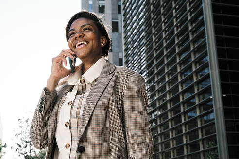 Happy businesswoman talking through smart phone on sunny day - AGOF00236