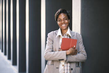 Happy businesswoman with tablet PC standing by wall - AGOF00239