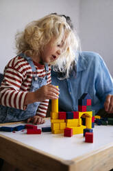 Son playing with toy blocks on table by father at home - ASGF02127