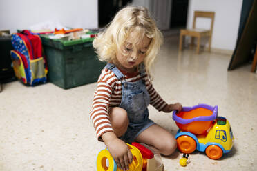 Blonder Junge spielt mit Spielzeugautos auf dem Boden zu Hause - ASGF02137