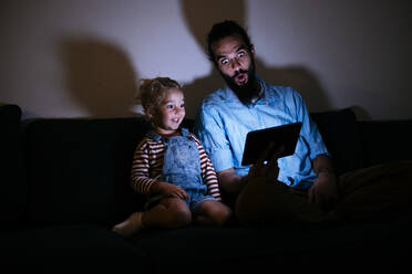 Vater und Sohn schauen gemeinsam im Wohnzimmer auf einen Tablet-PC - ASGF02142