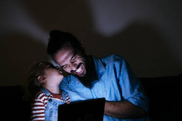 Son whispering in happy father's ear in front of tablet PC at home - ASGF02143