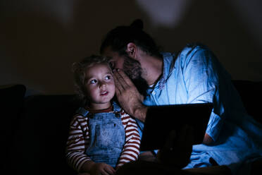 Vater mit Tablet-Computer, der seinem Sohn zu Hause ins Ohr flüstert - ASGF02144