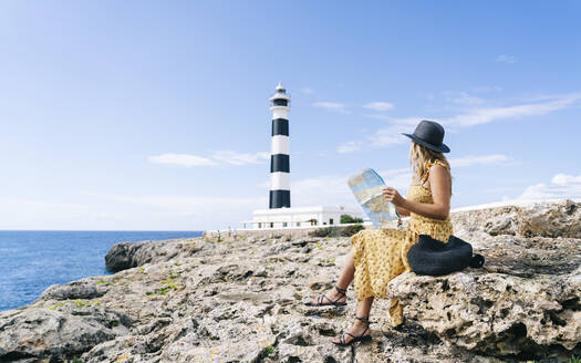 Tourist mit Landkarte auf einem Felsen am Leuchtturm von Artrutx auf Menorca, Spanien - DGOF02282