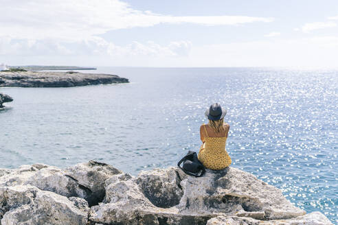 Frau sitzt auf einem Felsen und betrachtet das Meer an einem sonnigen Tag, Menorca, Spanien - DGOF02286