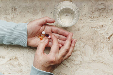 Senior woman taking medicinal pills with glass of water - IHF00756