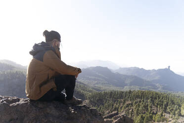 Mann sitzt auf einem Felsen und betrachtet die Aussicht an einem sonnigen Tag - ASGF02165