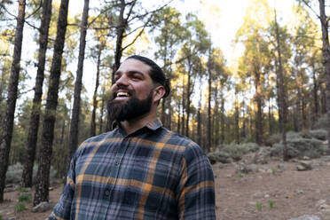 Happy man with beard standing in of forest - ASGF02170