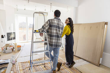 Young couple looking at living room being renovated inside new home - EIF03322