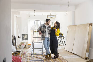 Young couple renovating home standing by ladder in living room - EIF03325