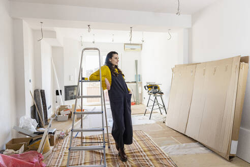 Nachdenkliche Frau, die sich im neuen Wohnzimmer auf eine Leiter stützt - EIF03332