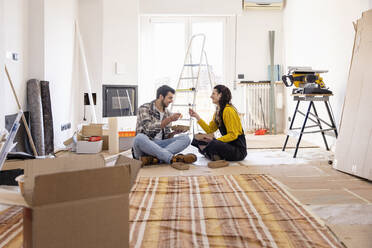 Young couple eating food sitting on ground at new home - EIF03343