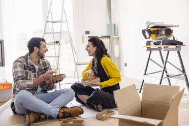 Cheerful young couple having food together at new home - EIF03347