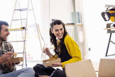 Happy man having sushi with girlfriend at living room at new home - EIF03348