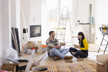 Young couple laughing and having food in living room - EIF03349