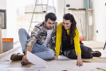 Smiling woman discussing over floor plans with boyfriend at new home - EIF03351