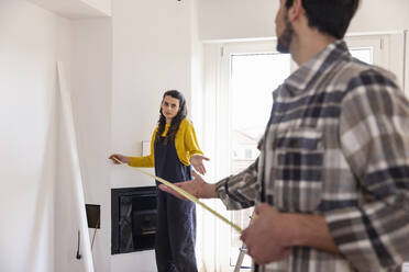 Confused woman with measuring tape talking with boyfriend in new living room - EIF03371