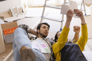 Junges Paar mit auf dem Boden liegenden Farbmustern in der neuen Wohnung - EIF03374