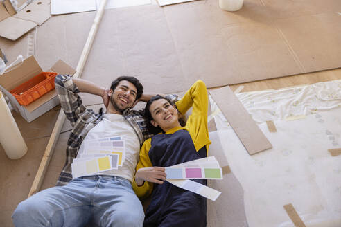 Glückliches Paar träumt mit Farbmustern, die im neuen Wohnzimmer auf dem Boden liegen - EIF03375