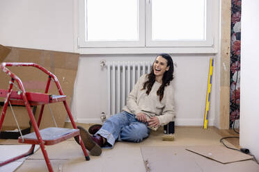 Happy woman sitting on ground at new home - EIF03396