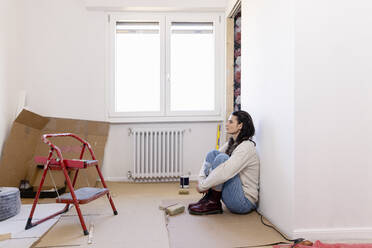 Thoughtful woman sitting on floor at home renovation work - EIF03397