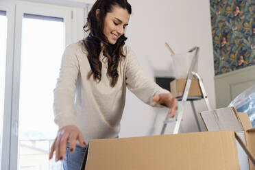 Smiling woman unpacking carboard boxes moving into new home - EIF03399