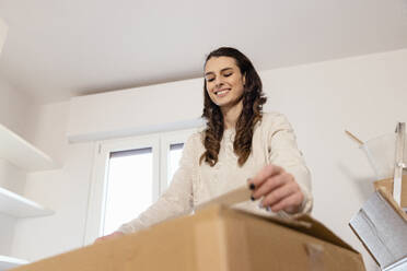 Lächelnde Frau, die einen Karton mit Klebeband verpackt und in ein neues Haus umzieht - EIF03403