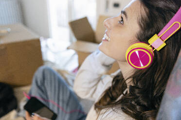 Junge Frau hört Musik über Kopfhörer und zieht in ein neues Haus um - EIF03407