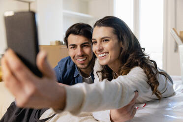 Lächelndes Paar macht Selfie mit Smartphone im Schlafzimmer des neuen Hauses - EIF03409