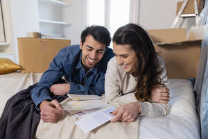 Lächelndes junges Paar bei der Auswahl von Farbmustern im Schlafzimmer des neuen Hauses - EIF03410