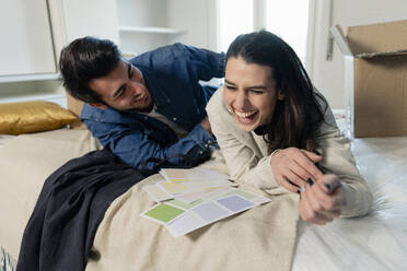 Cheerful young couple choosing color swatches in bedroom at new home - EIF03411