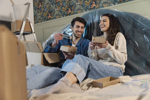 Glückliches Paar isst Sushi auf dem Bett sitzend im neuen Haus - EIF03412