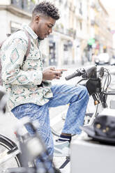 Mann mit Mobiltelefon auf einem Elektrofahrrad sitzend an einer Parkstation - IFRF01563