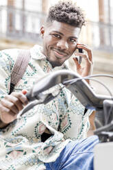 Lächelnder Mann, der an einer Fahrradabstellanlage mit seinem Smartphone telefoniert - IFRF01564