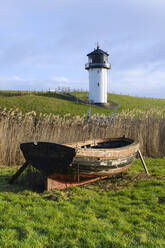 Germany, Lower Saxony, Cuxhaven, Old rowboat wth reeds and Dicke Berta lighthouse in background - WIF04488
