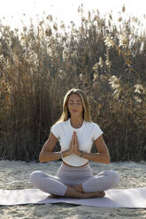 Frau in Meditationshaltung auf Yogamatte am Strand - TYF00102