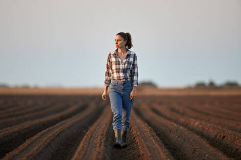 Junger Bauer geht bei Sonnenuntergang auf einem Feld spazieren - NOF00443