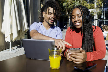 Young man talking with girlfriend using smart phone at sidewalk cafe - RFTF00167