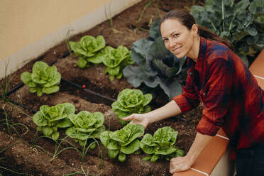 Smiling woman touching fresh green winter vegetables at courtyard garden - DMGF00662