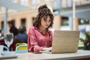 Junge Geschäftsfrau arbeitet am Laptop in einem Straßencafé - JCCMF05356