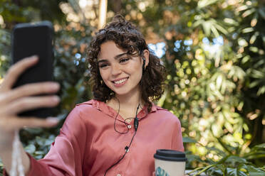 Glückliche Frau nimmt Selfie durch Smartphone im Garten - JCCMF05369