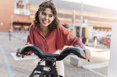 Glückliche Frau auf einem Elektrofahrrad am Bahnhof - JCCMF05390