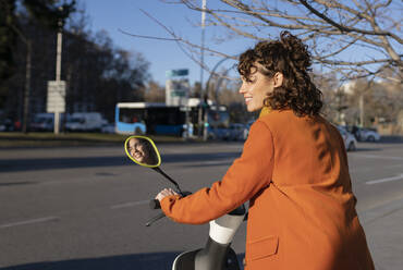 Lächelnde Frau mit Elektroroller auf der Straße - JCCMF05400