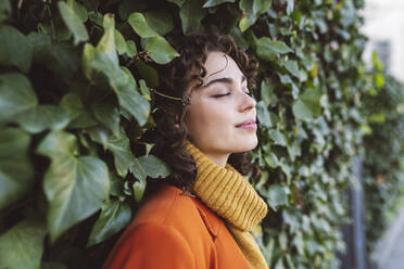 Young woman with eyes closed leaning on ivy wall - JCCMF05415