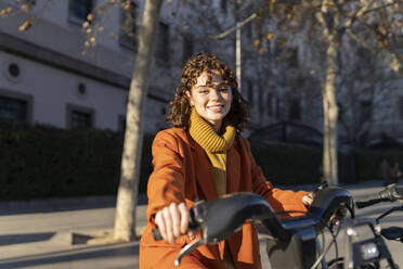 Smiling woman with electric bicycle on street - JCCMF05418