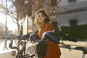 Happy woman with electric bicycle on footpath - JCCMF05419