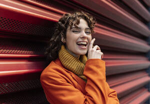 Cheerful woman near red corrugated wall - JCCMF05425