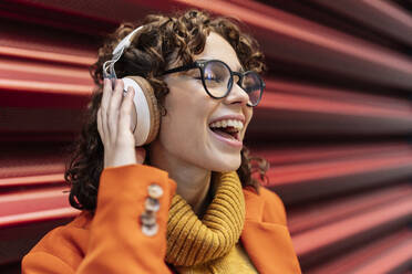 Happy woman listening music through headphones by wall - JCCMF05426